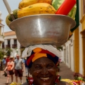 Colombian woman smiling as she carries a bowl of fruit on her head